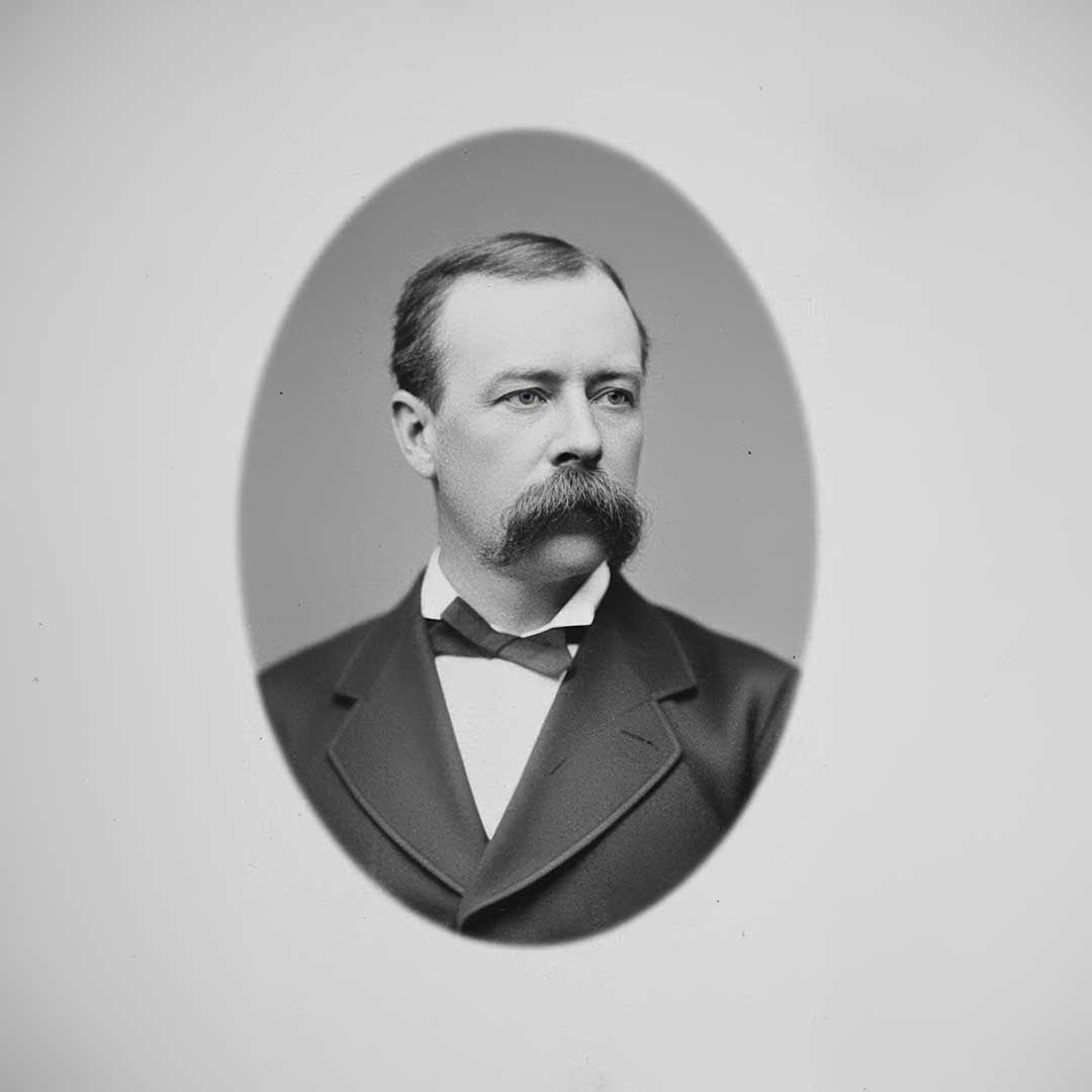 Formal black-and-white oval portrait of John W. Madden wearing a dark suit, white shirt, and bow tie, facing slightly to the viewer's left against a light studio background.